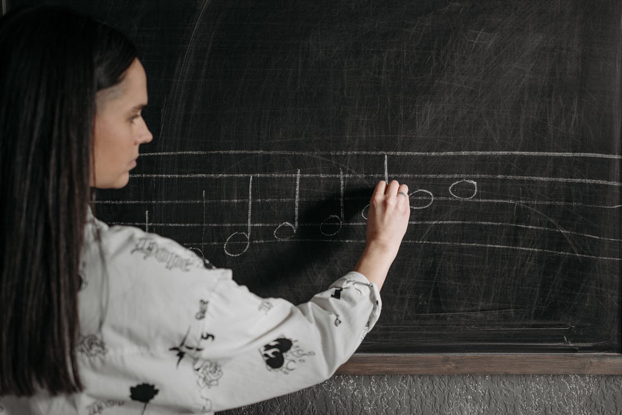A woman writing music notation on a blackboard during a lesson.