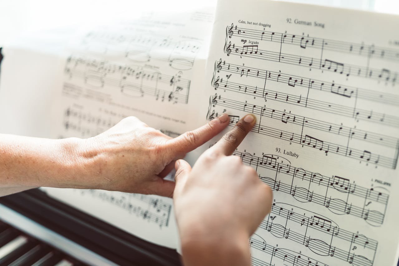 Close-up of hands pointing to notes on a music sheet during a piano lesson, highlighting music education.
